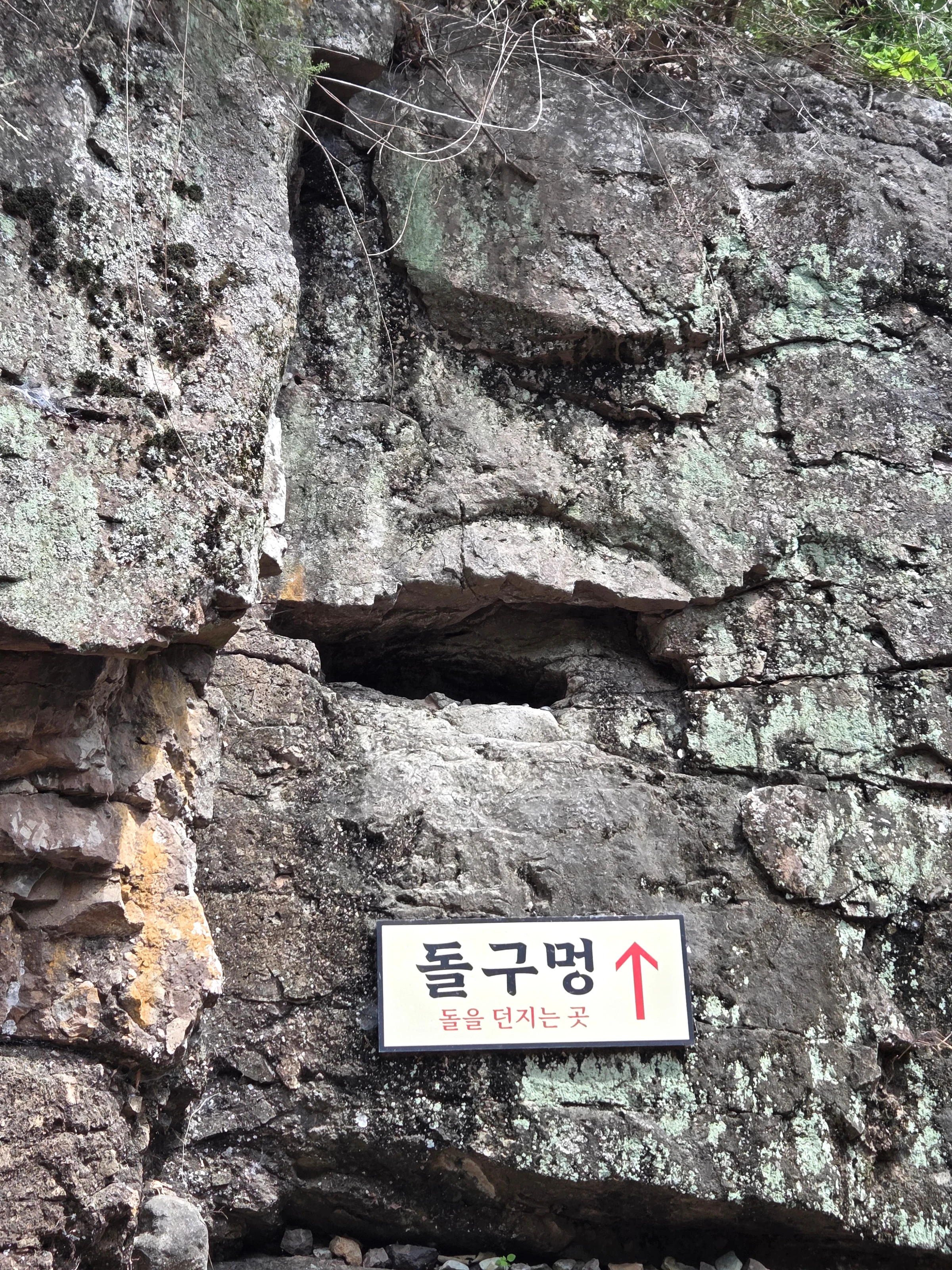 '돌구멍' 표지가 붙은 바위 절벽. 절벽 가운데 돌을 던져 넣는 구멍이 뚫려 있다.